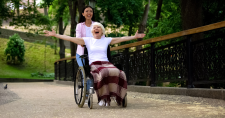 Long-Term Happiness. Picture of an elderly caucasian smiling female in a wheel chair, being pushed by a young asian smiling female.