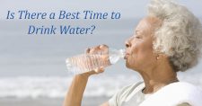 Timing Your Water Intake for Best Effects. Picture of an older black female drinking from a bottle of water while at the beach.